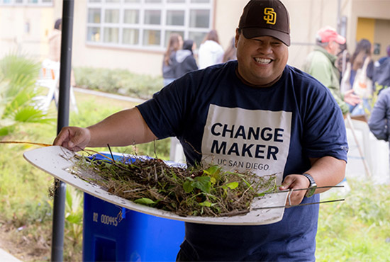 Smiling UCSD student holds gardening basket as they work on a local elementary school cleanup project