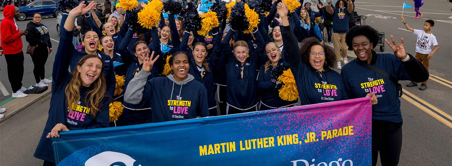 Smiling and laughing UC San Diego students march in the annual Martin Luther King Jr Day parade, holding a school banner